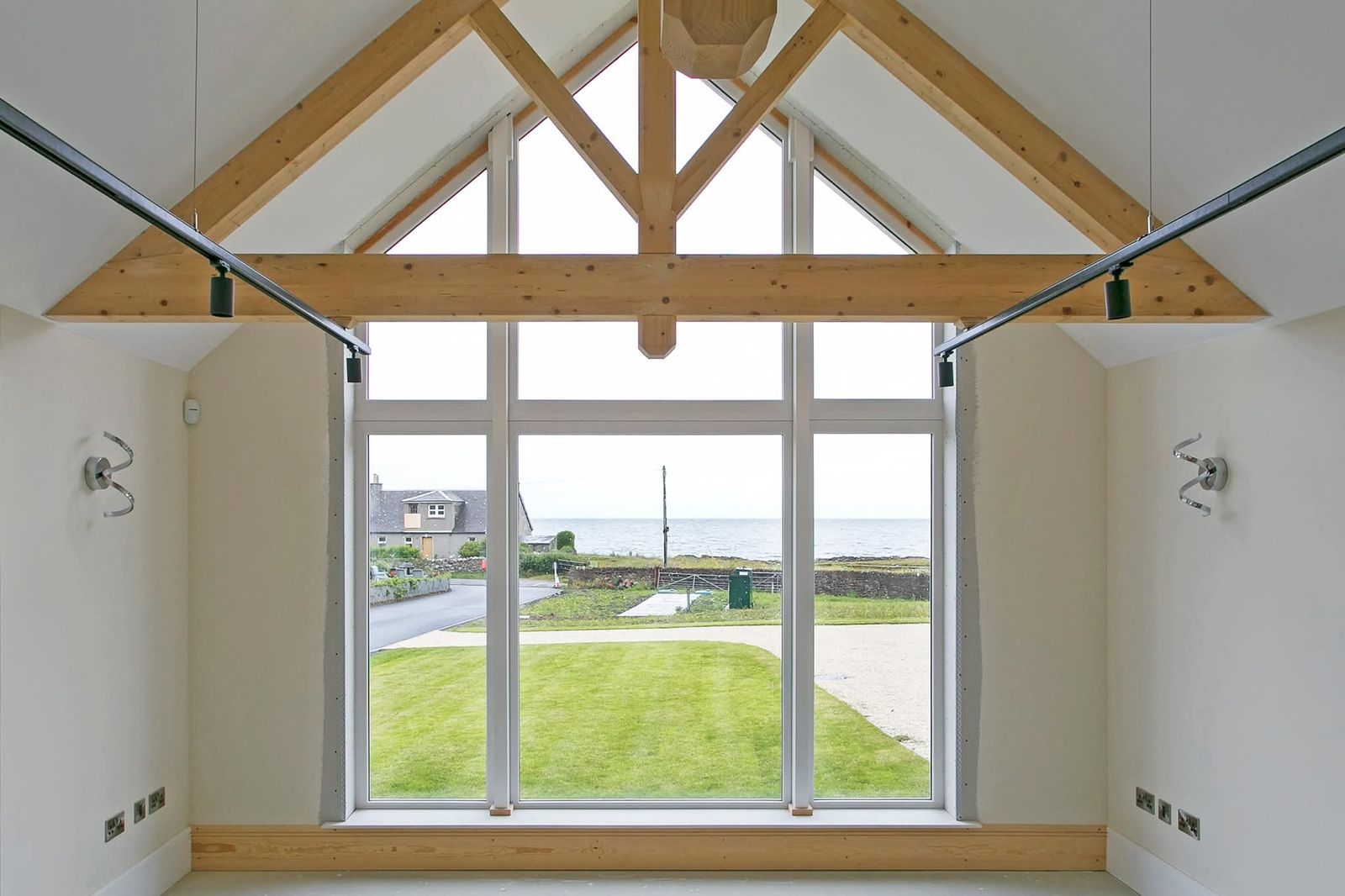Vaulted room in the finished house with exposed timber collar trusses and a full-height glazed gable looking out over a lawn to the sea