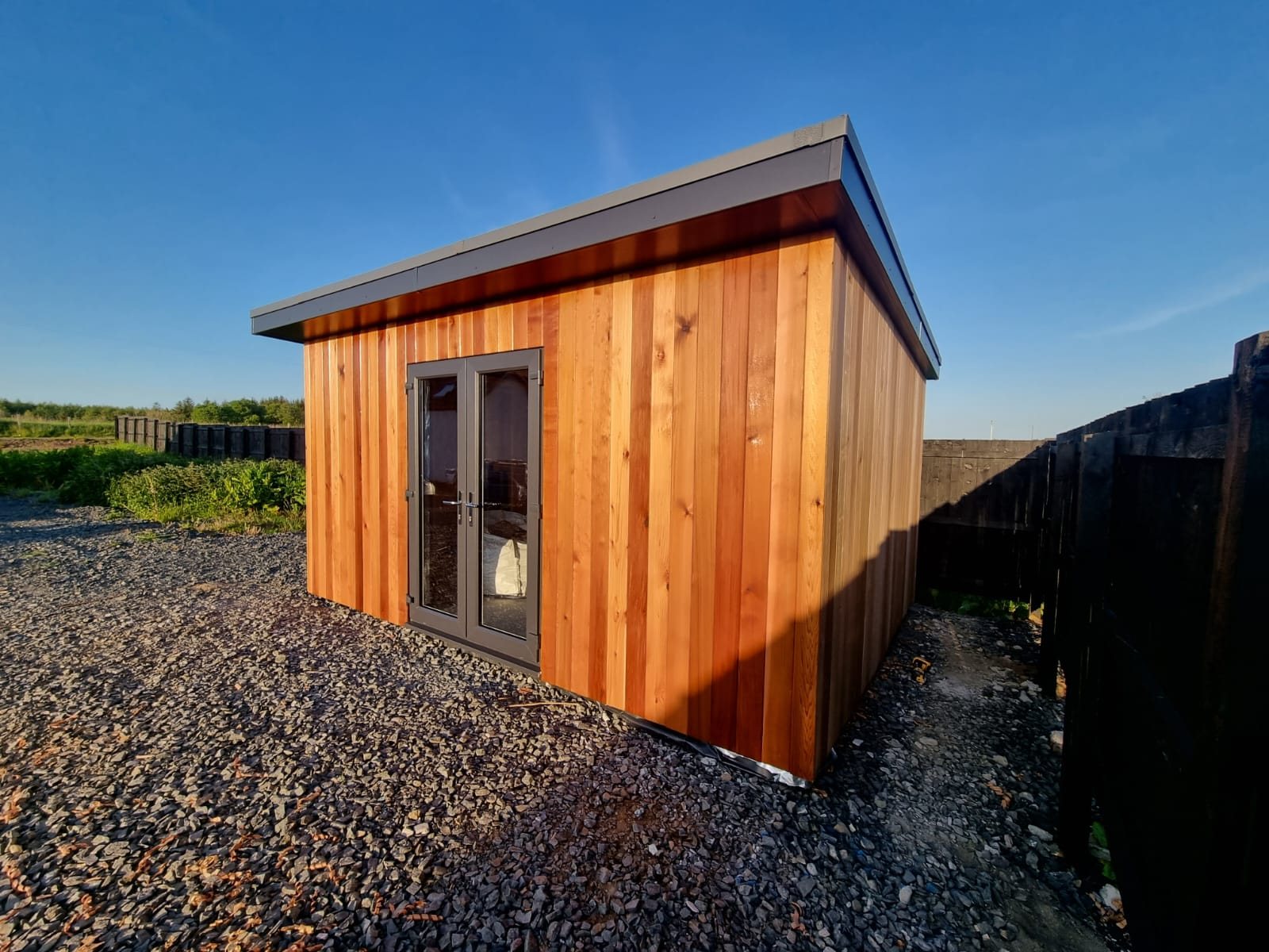 Finished single-storey garden room with vertical timber cladding, grey-framed glazed double doors and a gravel base